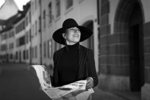 Woman in black hat on street holding newspaper